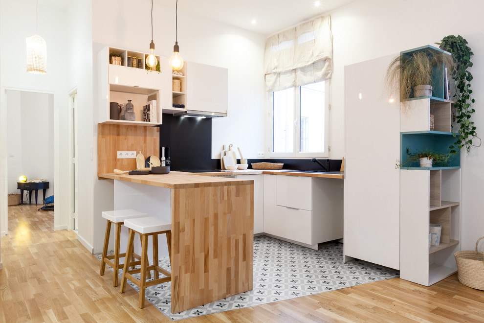 Küche in U-Form mit flächenbündigen Schrankfronten, weißen Schränken, Arbeitsplatte aus Holz, Küchenrückwand in Schwarz, Zementfliesen für Boden, Halbinsel und buntem Boden in Paris
