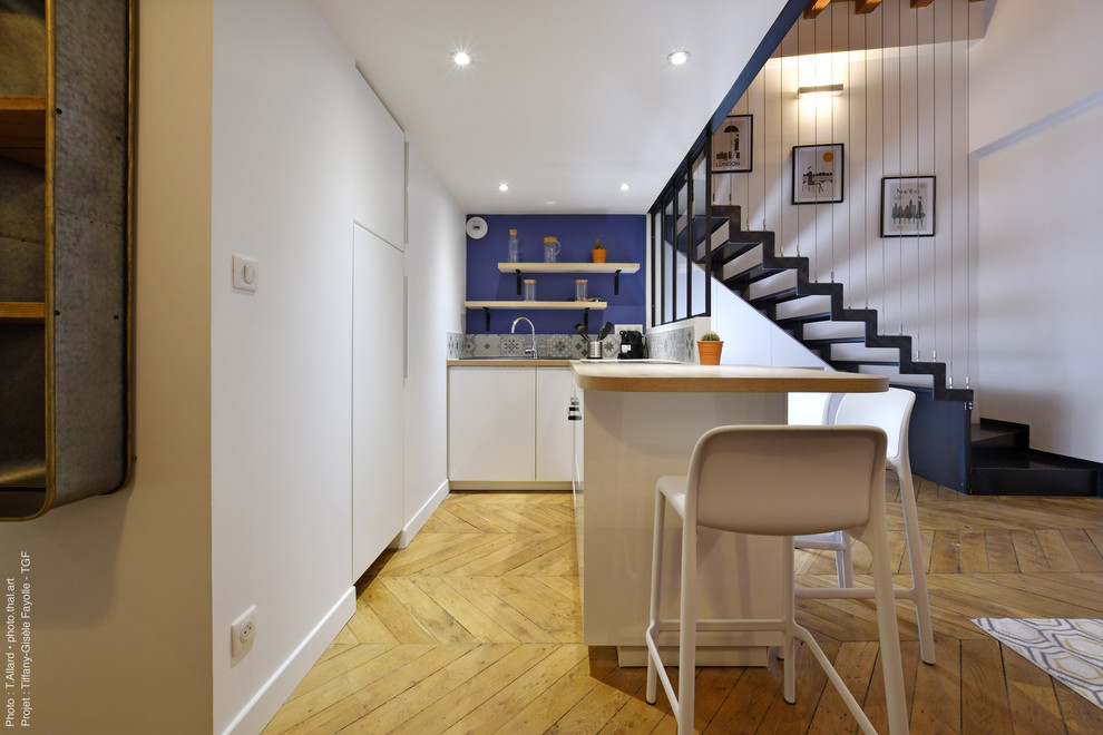 Photo of a small industrial l-shaped open plan kitchen in Lyon with an integrated sink, recessed-panel cabinets, white cabinets, laminate countertops, grey splashback, cement tile splashback, stainless steel appliances, light hardwood flooring, an island, beige floors and beige worktops.