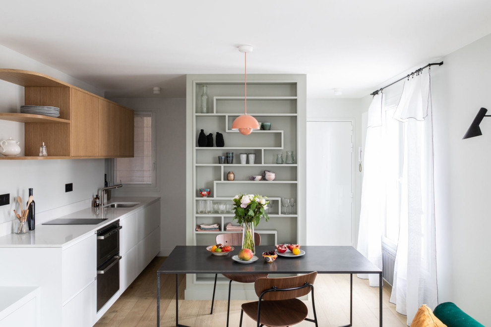 Inspiration for a small contemporary single-wall open plan kitchen in Paris with a submerged sink, beaded cabinets, white cabinets, granite worktops, white splashback, granite splashback, black appliances, light hardwood flooring, no island, beige floors and white worktops.