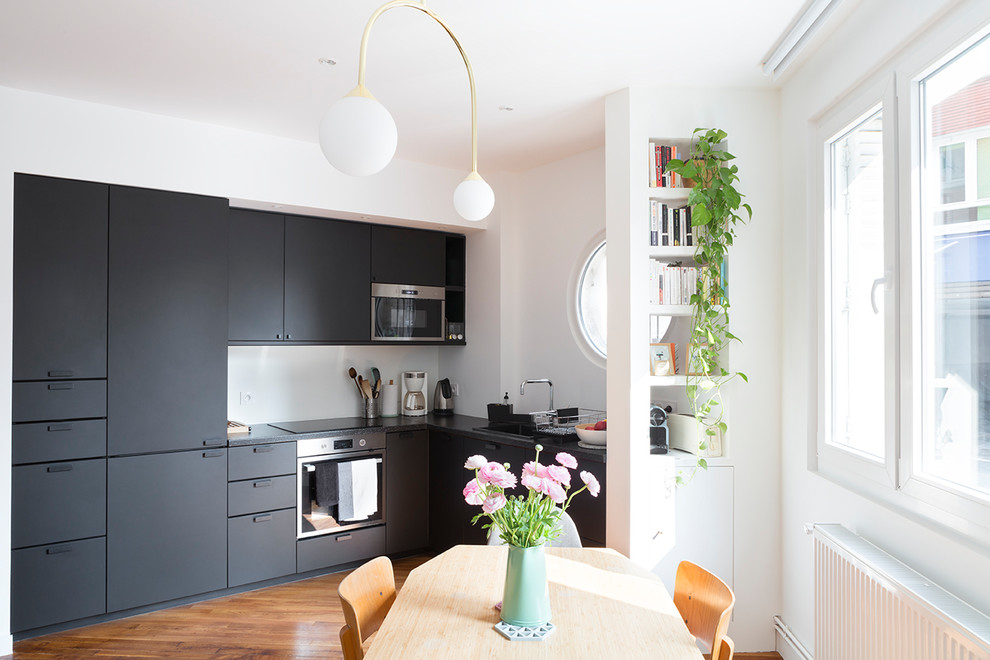 Mittelgroße Moderne Wohnküche in L-Form mit Unterbauwaschbecken, schwarzen Schränken, Laminat-Arbeitsplatte, braunem Holzboden und schwarzer Arbeitsplatte in Paris