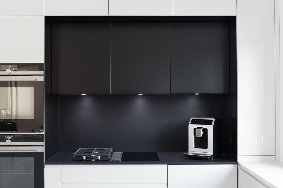 Foto på ett mellanstort svart kök, med en undermonterad diskho, luckor med profilerade fronter, vita skåp, granitbänkskiva, svart stänkskydd, stänkskydd i skiffer, en köksö och vitt golv