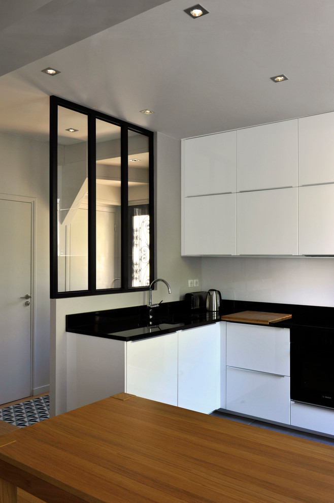 Idéer för att renovera ett mellanstort funkis svart svart kök, med en undermonterad diskho, luckor med profilerade fronter, vita skåp, svart stänkskydd, svarta vitvaror, ljust trägolv och brunt golv
