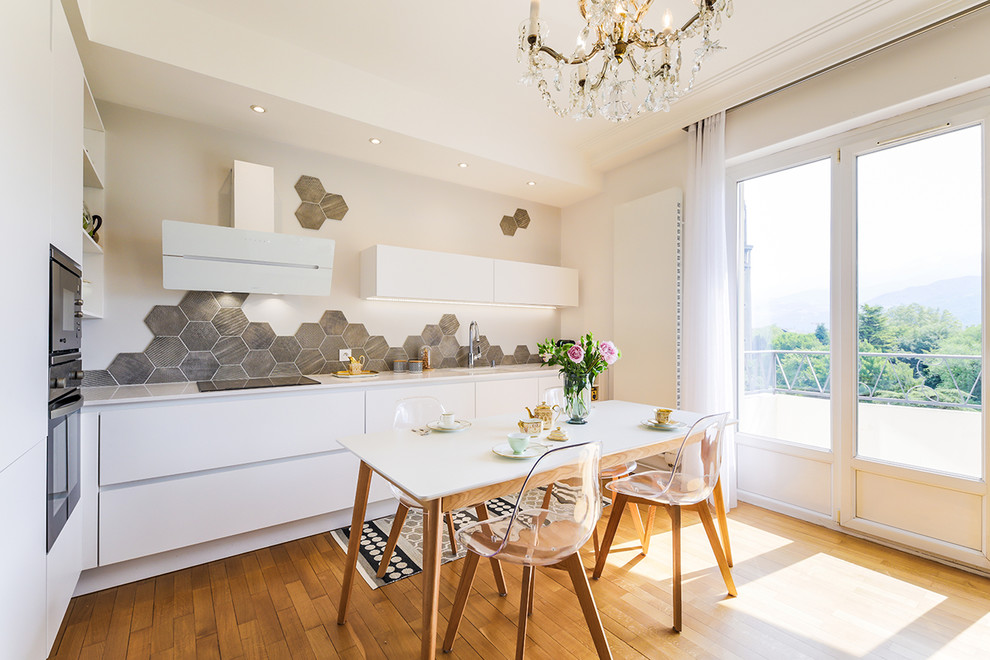 Skandinavische Wohnküche mit Waschbecken, flächenbündigen Schrankfronten, weißen Schränken, Küchenrückwand in Grau, hellem Holzboden und weißer Arbeitsplatte in Grenoble
