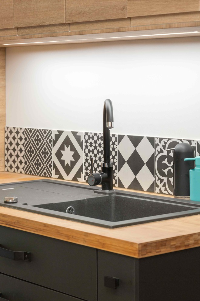 Cette image montre une grande cuisine ouverte parallèle design en bois brun avec un évier 1 bac, un plan de travail en bois, une crédence multicolore, une crédence en carreau de ciment, un électroménager noir et un sol en bois brun.