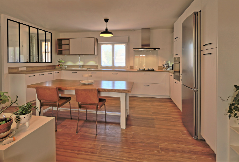 Inredning av ett lantligt stort brun brunt kök, med en undermonterad diskho, släta luckor, vita skåp, träbänkskiva, vitt stänkskydd, stänkskydd i glaskakel, rostfria vitvaror, klinkergolv i porslin, en köksö och brunt golv