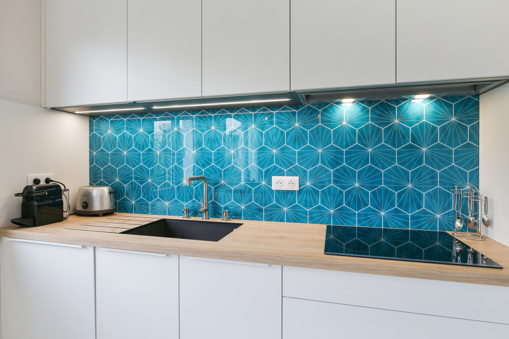 Inspiration for a large contemporary galley open plan kitchen in Other with a submerged sink, flat-panel cabinets, white cabinets, wood worktops, blue splashback, mosaic tiled splashback, integrated appliances, laminate floors, an island, grey floors and brown worktops.