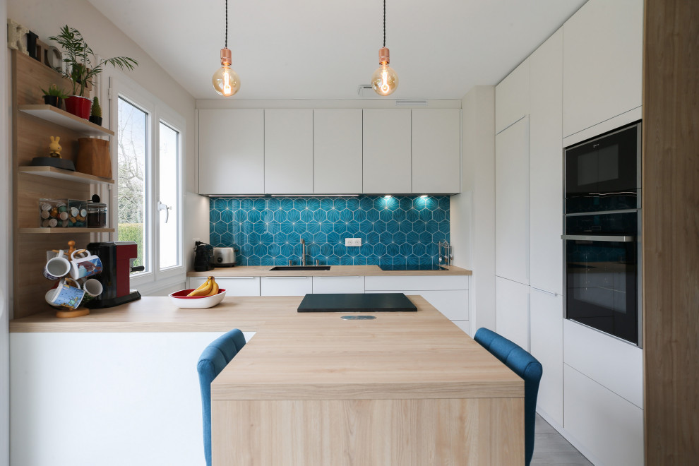 Inredning av ett modernt stort brun brunt kök, med en köksö, släta luckor, vita skåp, en undermonterad diskho, träbänkskiva, blått stänkskydd, stänkskydd i mosaik, integrerade vitvaror, laminatgolv och grått golv