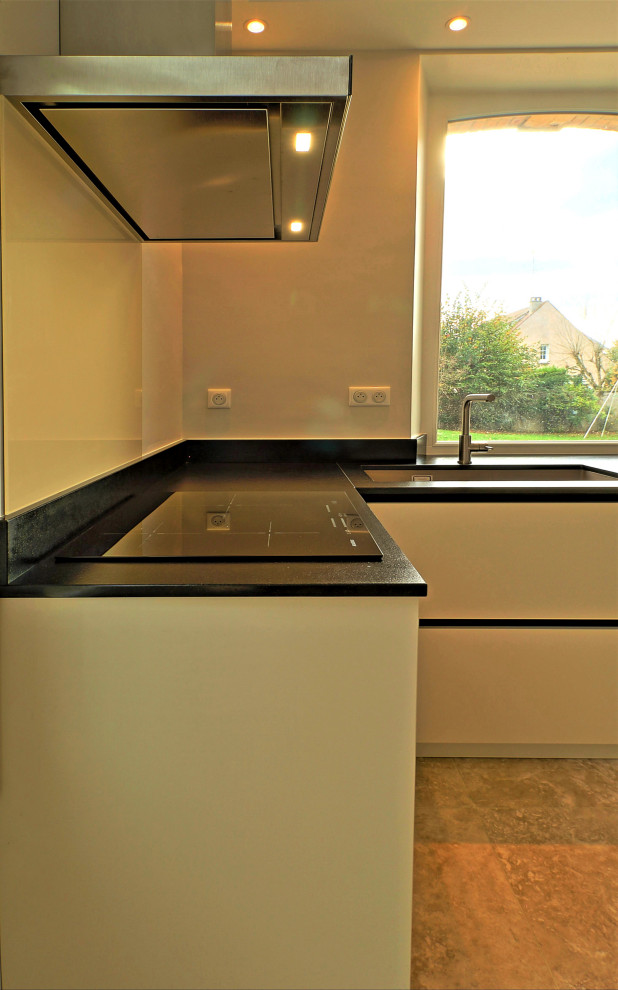 Immagine di una cucina moderna di medie dimensioni con lavello sottopiano, ante lisce, ante bianche, top in granito, paraspruzzi bianco, paraspruzzi in granito, elettrodomestici in acciaio inossidabile, pavimento in cementine, pavimento beige e top nero