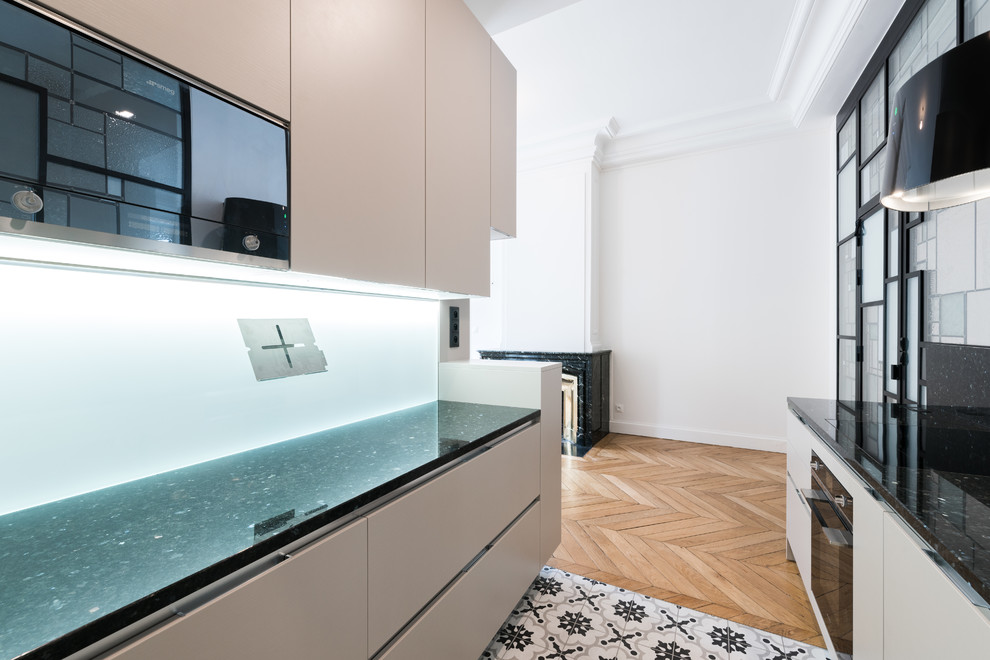 Small contemporary galley open plan kitchen in Lyon with an integrated sink, recessed-panel cabinets, beige cabinets, granite worktops, black splashback, cement tile splashback, black appliances, cement flooring and no island.