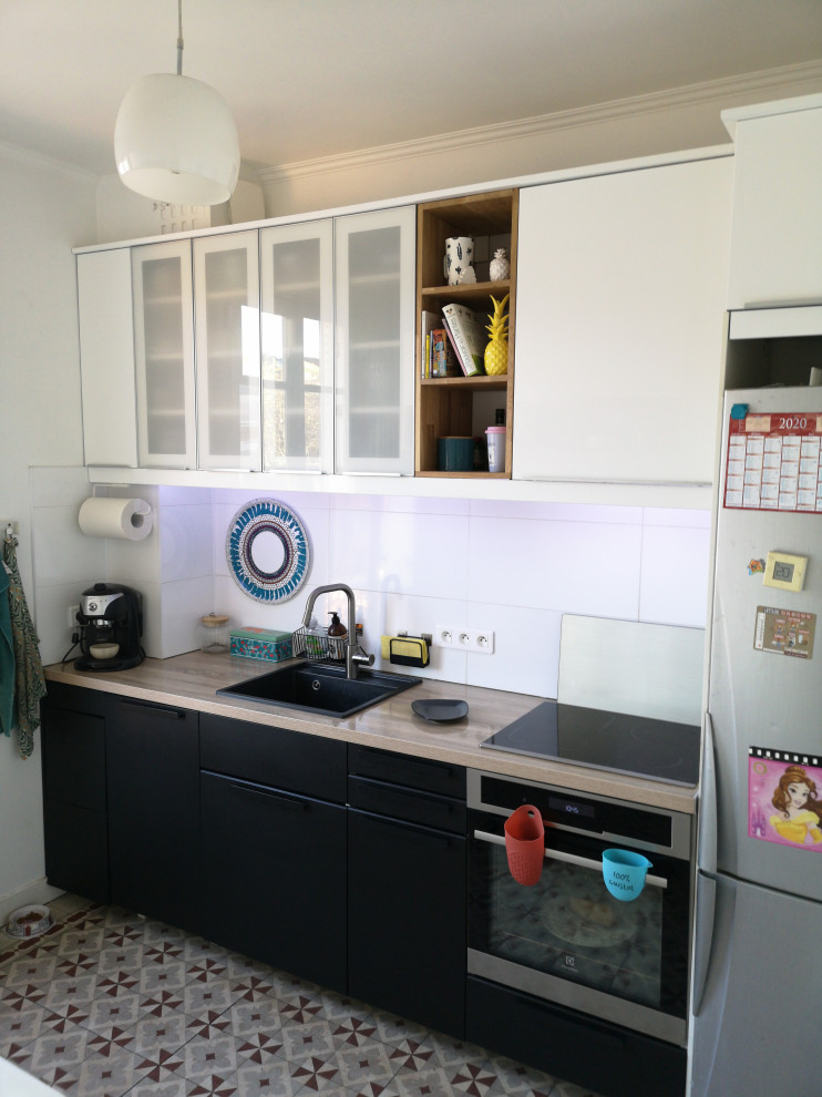 パリにある高級な中くらいなモダンスタイルのおしゃれなキッチン (シングルシンク、ガラス扉のキャビネット、黒いキャビネット、ラミネートカウンター、白いキッチンパネル、セラミックタイルのキッチンパネル、パネルと同色の調理設備、セメントタイルの床、アイランドなし、グレーの床、ベージュのキッチンカウンター) の写真
