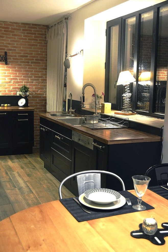Foto på ett industriellt beige kök, med en dubbel diskho, luckor med infälld panel, svarta skåp, träbänkskiva, svart stänkskydd, stänkskydd i keramik, rostfria vitvaror och en köksö