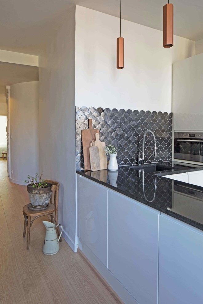 Inredning av ett modernt litet kök, med en integrerad diskho, luckor med profilerade fronter, vita skåp, granitbänkskiva, svart stänkskydd och stänkskydd i terrakottakakel