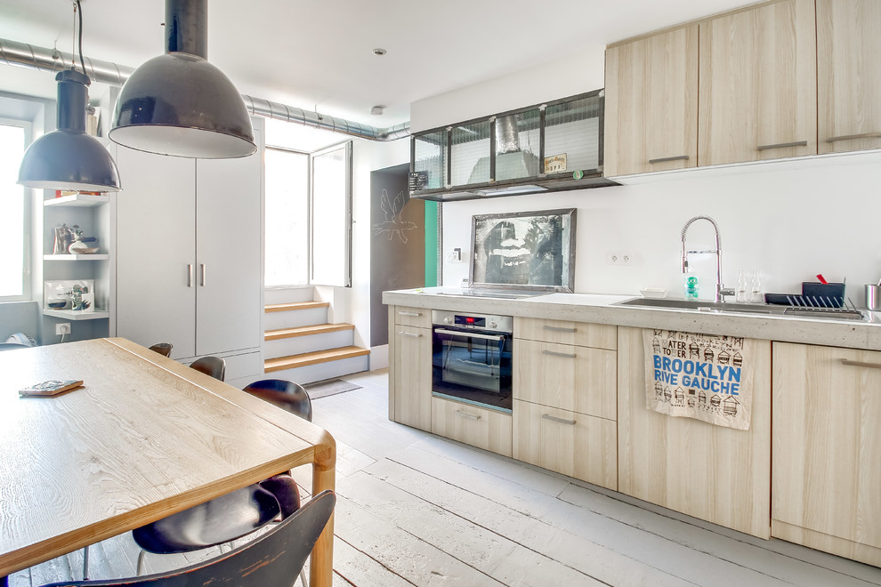 Cette image montre une cuisine américaine nordique en bois clair avec un placard à porte plane, un plan de travail en béton, parquet peint, un sol beige et un plan de travail gris.