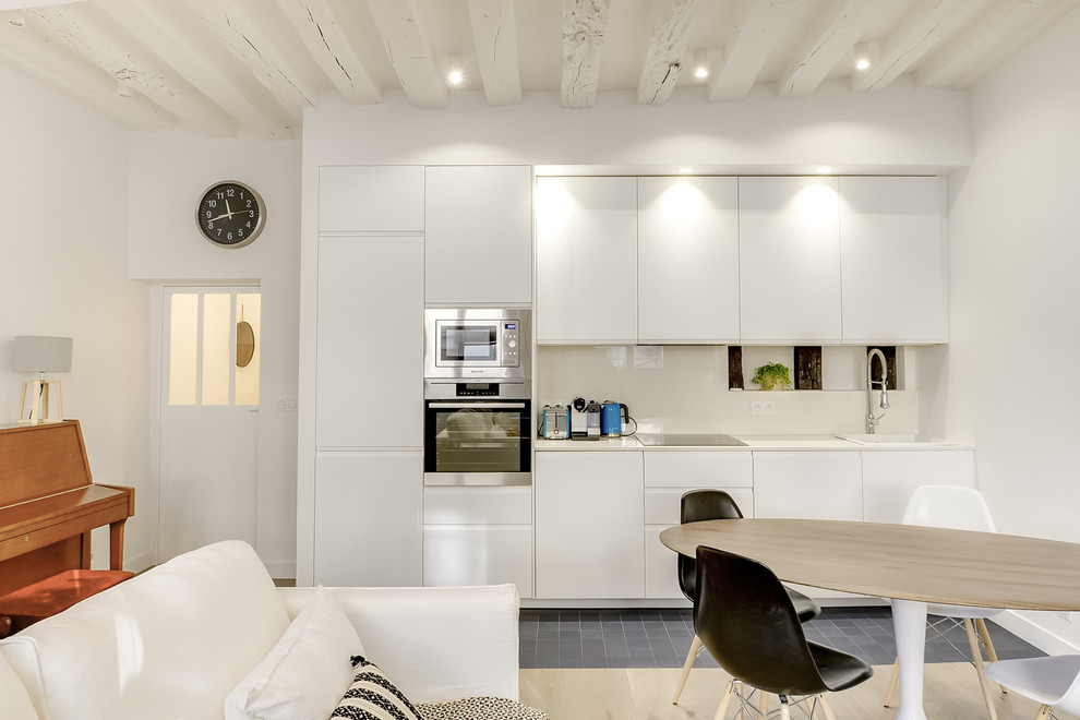 Inredning av ett modernt mellanstort linjärt kök med öppen planlösning, med en integrerad diskho, släta luckor, vita skåp, marmorbänkskiva, vitt stänkskydd, stänkskydd i marmor, integrerade vitvaror, cementgolv och svart golv