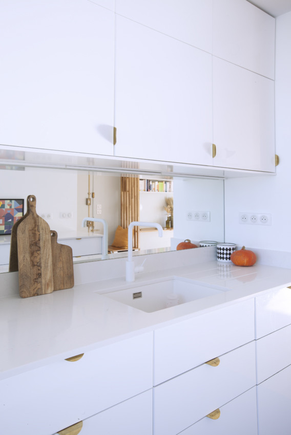Modern inredning av ett mellanstort vit vitt kök, med en undermonterad diskho, luckor med profilerade fronter, vita skåp, bänkskiva i kvartsit, stänkskydd med metallisk yta, spegel som stänkskydd, integrerade vitvaror, betonggolv och blått golv