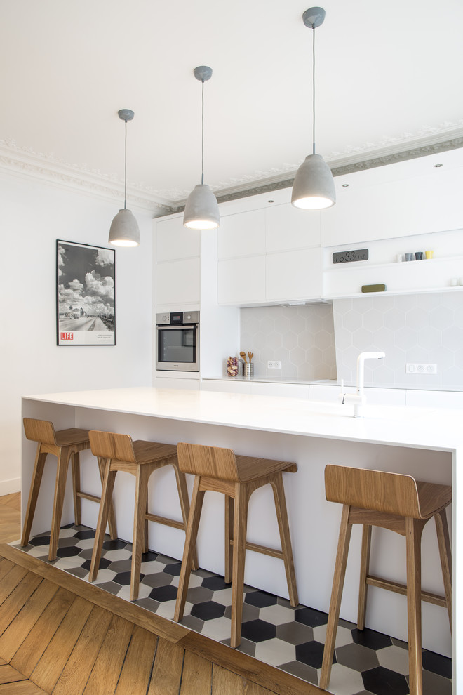 Photo of a large contemporary single-wall kitchen/diner in Paris with an integrated sink, flat-panel cabinets, white cabinets, grey splashback, stainless steel appliances, light hardwood flooring, multiple islands and white worktops.