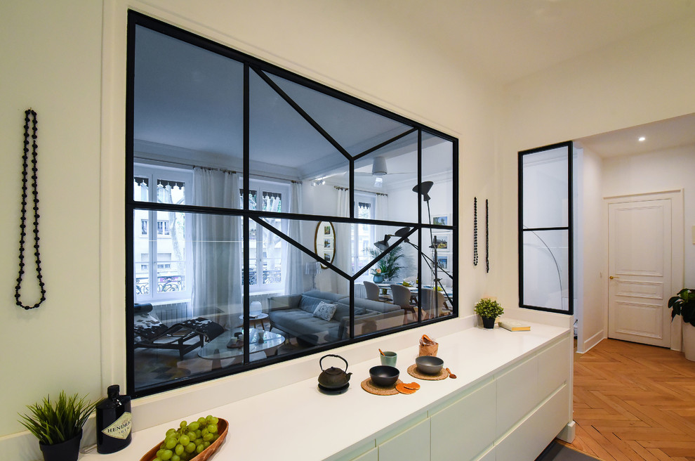 Cette image montre une cuisine design avec un placard à porte affleurante, des portes de placard blanches, une crédence blanche, un électroménager en acier inoxydable, un sol en bois brun, îlot et un sol beige.