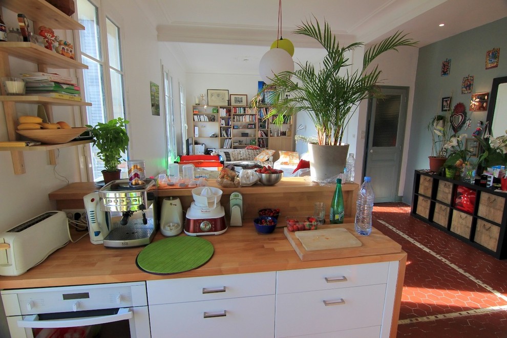 На фото: параллельная кухня среднего размера в современном стиле с обеденным столом, врезной мойкой, плоскими фасадами, белыми фасадами, деревянной столешницей, зеленым фартуком, фартуком из стекла, белой техникой, полом из терракотовой плитки и островом с