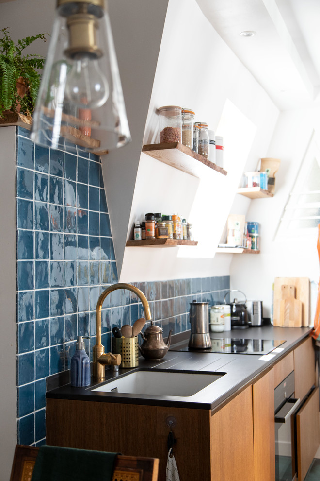 Источник вдохновения для домашнего уюта: маленькая параллельная кухня-гостиная в средиземноморском стиле с плоскими фасадами, светлыми деревянными фасадами, синим фартуком, фартуком из керамической плитки, черной техникой, полом из керамической плитки, синим полом, черной столешницей, врезной мойкой, столешницей из акрилового камня и полуостровом для на участке и в саду