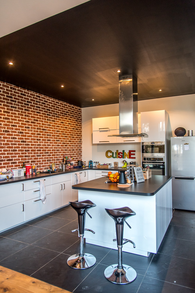 Large urban l-shaped slate floor and black floor eat-in kitchen photo in Paris with an undermount sink, white cabinets, brick backsplash, stainless steel appliances, an island and black countertops