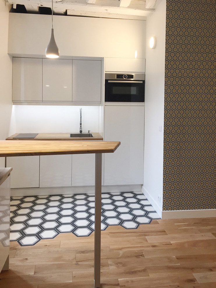 Exempel på ett litet nordiskt kök, med en undermonterad diskho, luckor med profilerade fronter, vita skåp, träbänkskiva, vitt stänkskydd, glaspanel som stänkskydd, rostfria vitvaror, cementgolv, en köksö och flerfärgat golv