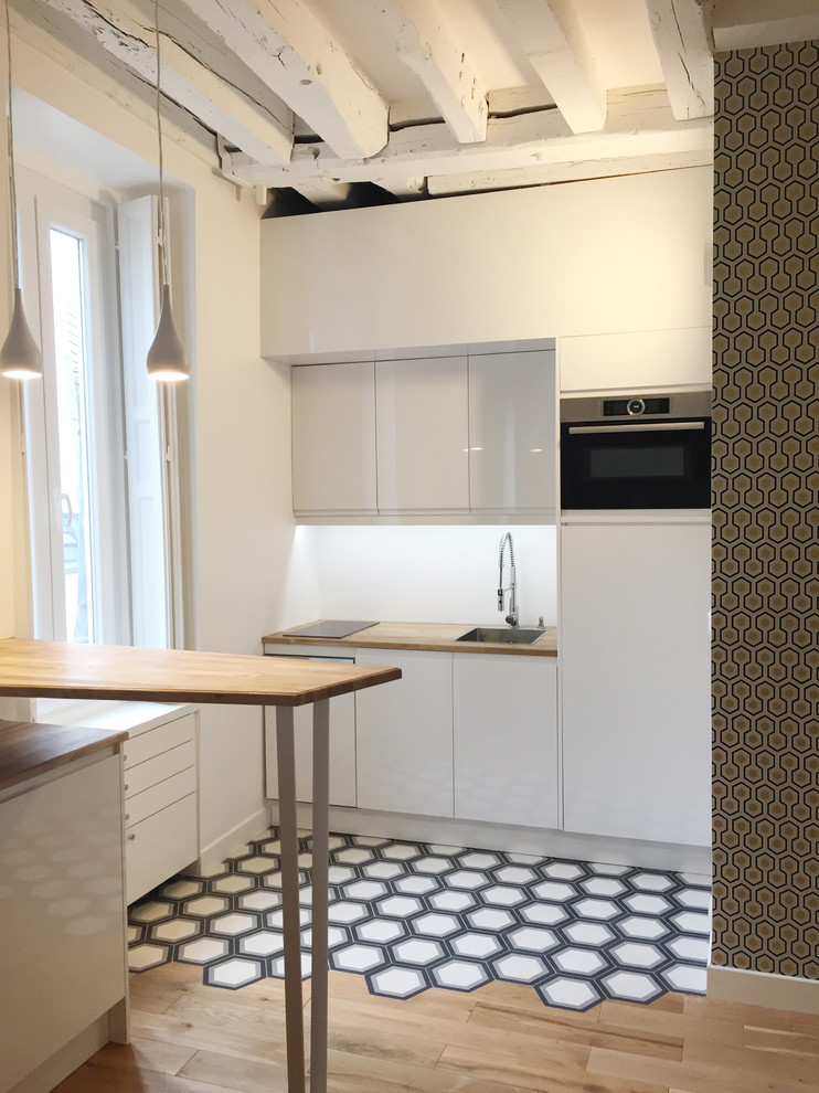 Inspiration för små minimalistiska kök, med en undermonterad diskho, luckor med profilerade fronter, vita skåp, träbänkskiva, vitt stänkskydd, glaspanel som stänkskydd, rostfria vitvaror, cementgolv, en köksö och flerfärgat golv