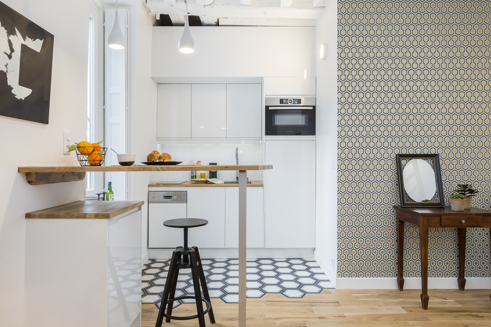 This is an example of a medium sized scandi single-wall kitchen in Paris with a built-in sink, flat-panel cabinets, white cabinets, wood worktops, white splashback, white appliances, a breakfast bar, brown worktops and light hardwood flooring.