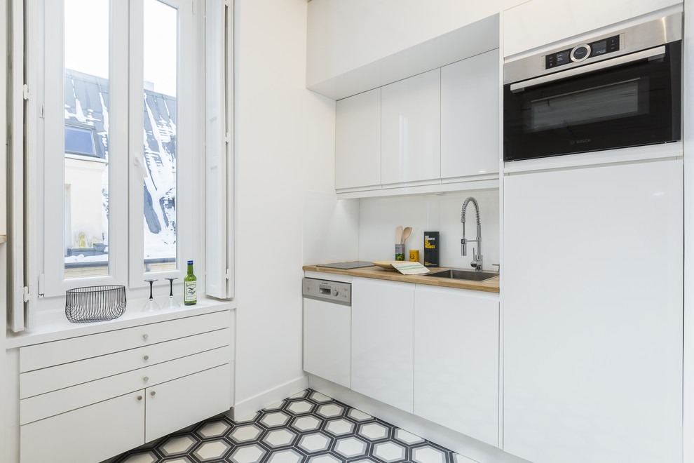 Idéer för att renovera ett litet minimalistiskt kök, med en undermonterad diskho, luckor med profilerade fronter, vita skåp, träbänkskiva, vitt stänkskydd, glaspanel som stänkskydd, rostfria vitvaror, cementgolv, en köksö och flerfärgat golv