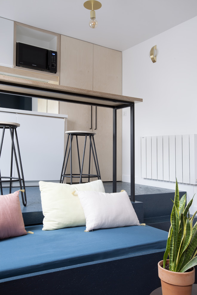 パリにある小さなコンテンポラリースタイルのおしゃれなキッチン (シングルシンク、フラットパネル扉のキャビネット、淡色木目調キャビネット、木材カウンター、黒いキッチンパネル、ガラス板のキッチンパネル、黒い調理設備、コンクリートの床、青い床) の写真