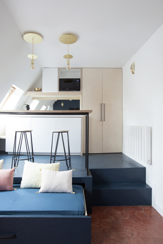 Design ideas for a small contemporary galley open plan kitchen in Paris with a single-bowl sink, flat-panel cabinets, light wood cabinets, wood worktops, black splashback, glass sheet splashback, black appliances, concrete flooring, a breakfast bar and blue floors.