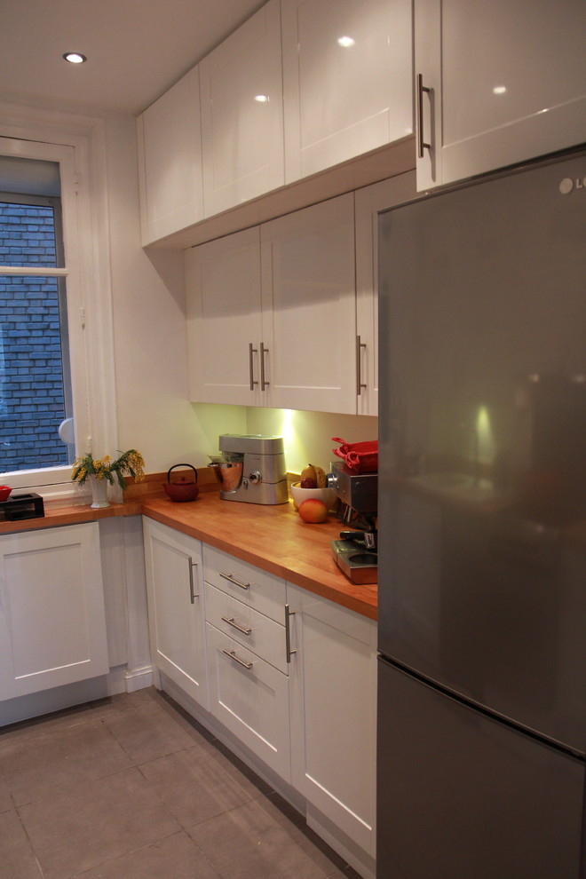 Photo of a small traditional u-shaped enclosed kitchen in Paris with a built-in sink, flat-panel cabinets, white cabinets, wood worktops, beige splashback, wood splashback, stainless steel appliances, ceramic flooring, no island and grey floors.