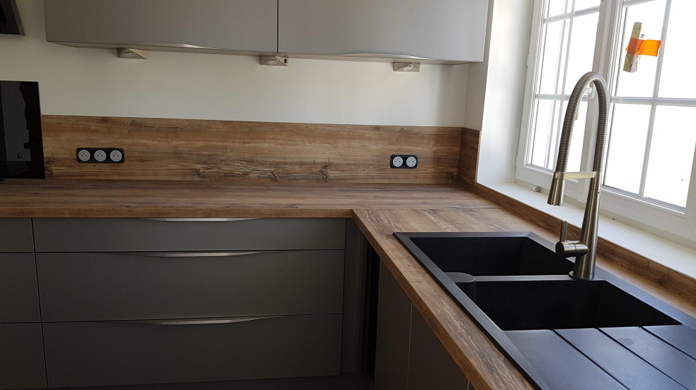 Example of a mid-sized minimalist l-shaped ceramic tile and black floor enclosed kitchen design in Lille with a double-bowl sink, beaded inset cabinets, gray cabinets, wood countertops, wood backsplash, black appliances and an island
