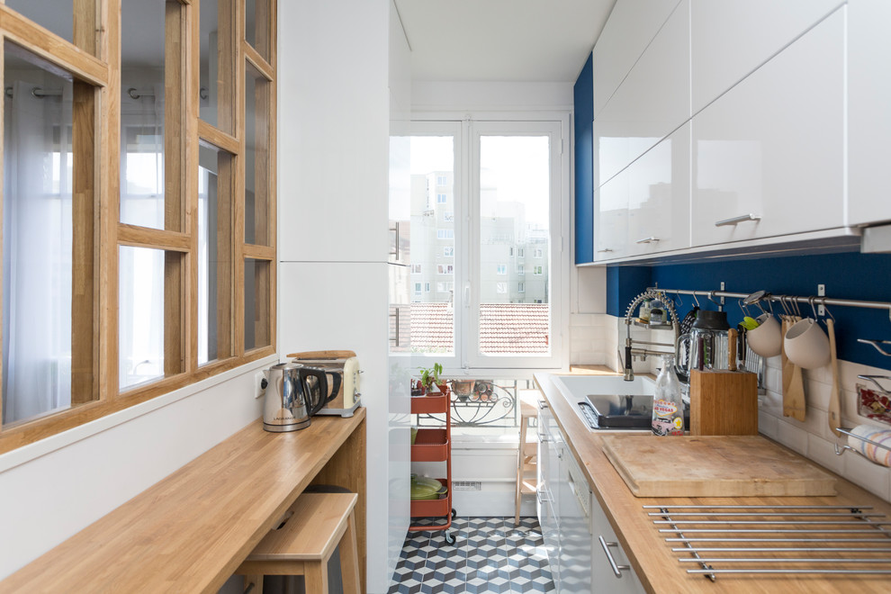 Foto på ett avskilt skandinaviskt linjärt kök, med en nedsänkt diskho, släta luckor, vita skåp, träbänkskiva, vitt stänkskydd, stänkskydd i tunnelbanekakel, vita vitvaror, flerfärgat golv och cementgolv