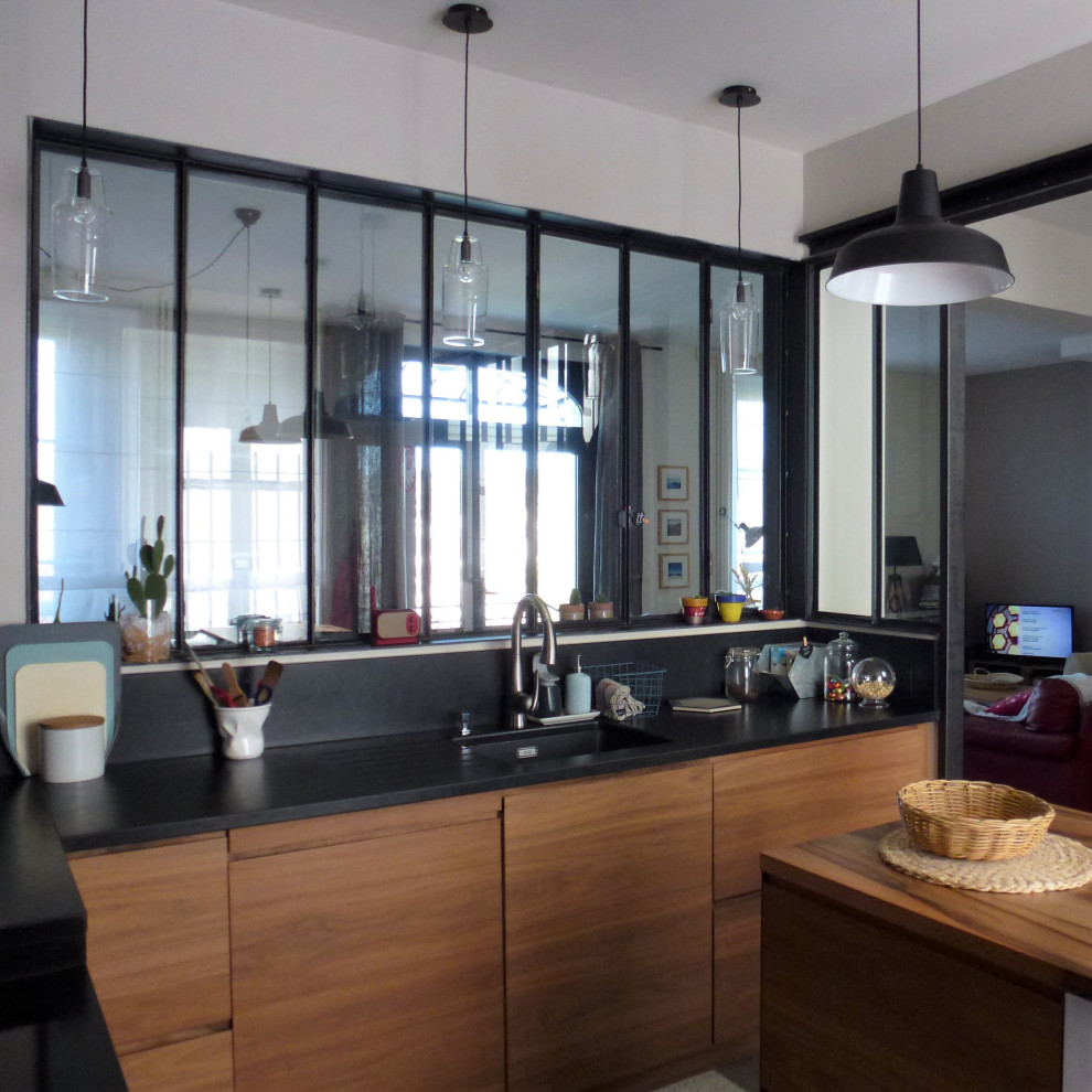 This is an example of a medium sized industrial l-shaped enclosed kitchen in Clermont-Ferrand with beaded cabinets, light wood cabinets, granite worktops, black splashback, granite splashback, cement flooring, an island, grey floors and black worktops.