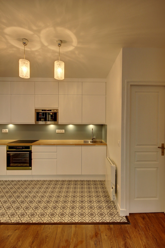 Immagine di una cucina scandinava di medie dimensioni con lavello sottopiano, ante bianche, top in legno, paraspruzzi blu, elettrodomestici da incasso e pavimento in laminato