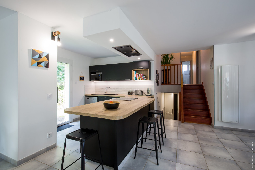 Exempel på ett mellanstort modernt brun brunt kök, med en enkel diskho, luckor med profilerade fronter, svarta skåp, träbänkskiva, vitt stänkskydd, stänkskydd i tunnelbanekakel, en köksö och grått golv