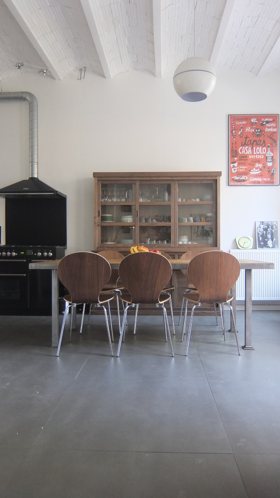 Bild på ett stort industriellt kök, med en enkel diskho, öppna hyllor, skåp i rostfritt stål, kaklad bänkskiva, grått stänkskydd, stänkskydd i keramik, svarta vitvaror, betonggolv och en köksö