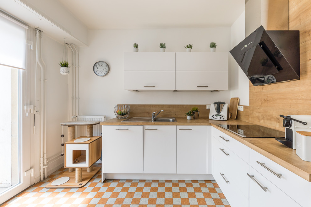 Modern inredning av ett l-kök, med en nedsänkt diskho, släta luckor, vita skåp, träbänkskiva, stänkskydd i trä, svarta vitvaror och orange golv