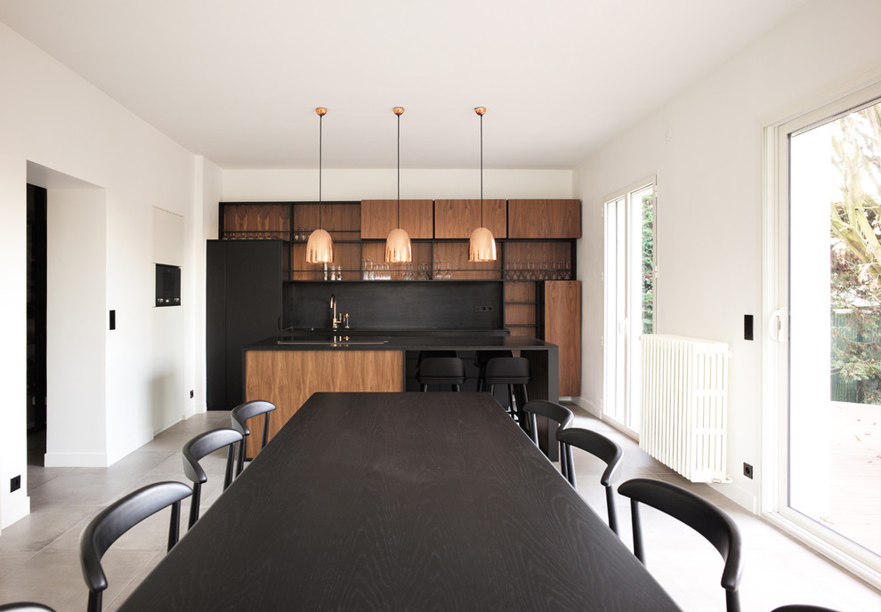 Large contemporary single-wall open plan kitchen in Paris with a submerged sink, beaded cabinets, black cabinets, composite countertops, black splashback, black appliances, ceramic flooring, an island, grey floors and black worktops.