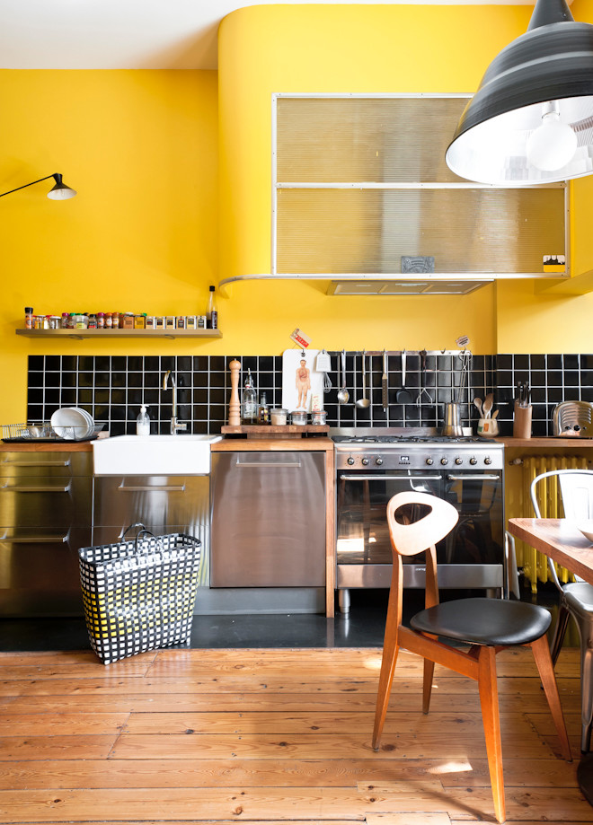Einzeilige, Mittelgroße Moderne Wohnküche mit Landhausspüle, Edelstahlfronten, Küchenrückwand in Schwarz, bunten Elektrogeräten und braunem Holzboden in Bordeaux