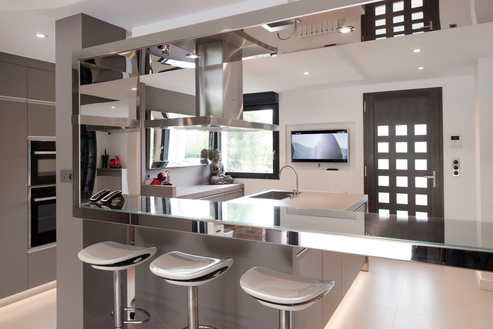 Cette image montre une cuisine parallèle design avec un évier encastré, un placard à porte plane, des portes de placard grises, un électroménager noir, îlot, un sol gris et un plan de travail gris.