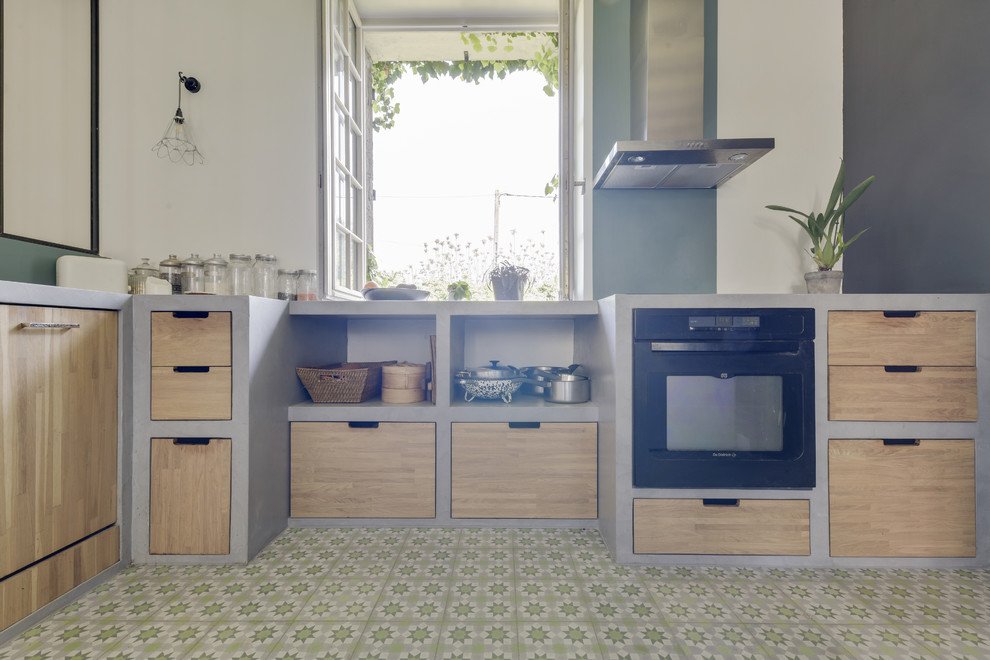 This is an example of a large mediterranean l-shaped enclosed kitchen in Paris with a belfast sink, open cabinets, light wood cabinets, concrete worktops, green splashback, black appliances, cement flooring, no island, green floors and grey worktops.