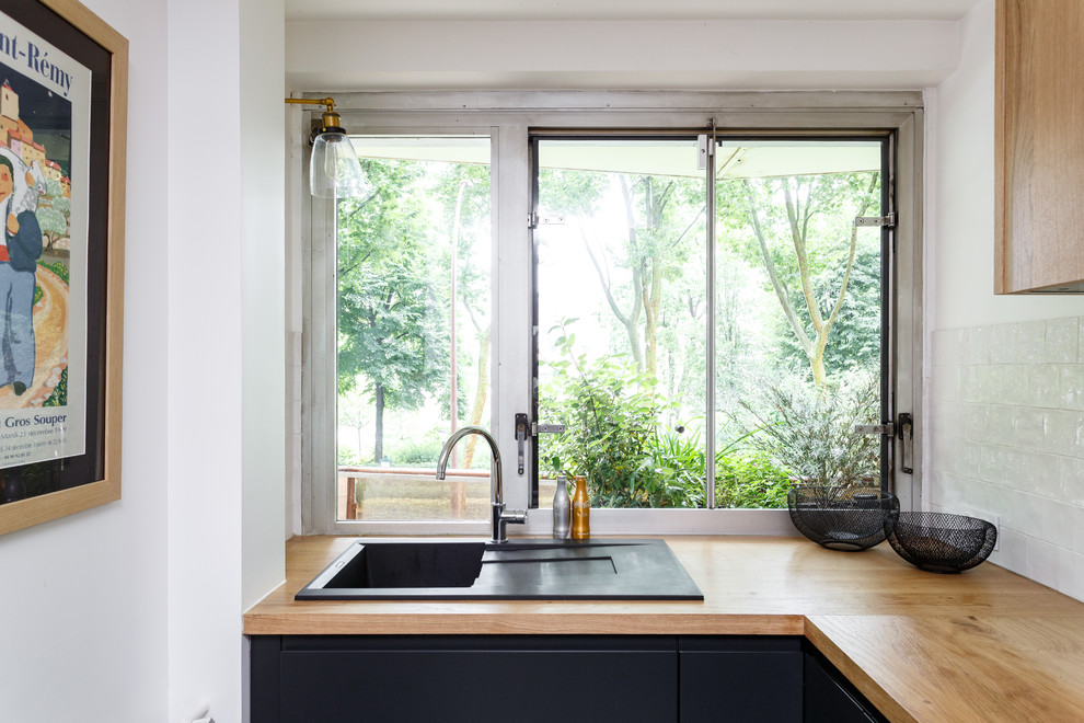 Foto på ett avskilt, litet skandinaviskt brun l-kök, med en nedsänkt diskho, släta luckor, svarta skåp, träbänkskiva, vitt stänkskydd, stänkskydd i keramik, rostfria vitvaror, terrazzogolv och flerfärgat golv