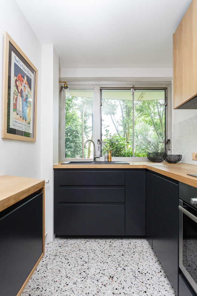 Inredning av ett skandinaviskt litet, avskilt brun brunt l-kök, med en nedsänkt diskho, släta luckor, svarta skåp, träbänkskiva, fönster som stänkskydd, flerfärgat golv, vitt stänkskydd, rostfria vitvaror och terrazzogolv