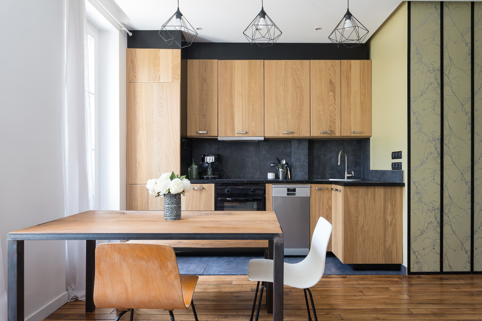 パリにあるコンテンポラリースタイルのおしゃれなキッチン (フラットパネル扉のキャビネット、中間色木目調キャビネット、パネルと同色の調理設備、無垢フローリング、アイランドなし、茶色い床、黒いキッチンカウンター) の写真