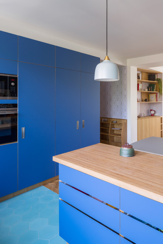 Modern inredning av ett mellanstort beige linjärt beige kök med öppen planlösning, med en enkel diskho, släta luckor, blå skåp, träbänkskiva, stänkskydd med metallisk yta, stänkskydd i trä, färgglada vitvaror, klinkergolv i keramik, en köksö och turkost golv