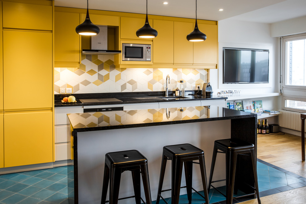 Foto på ett mellanstort skandinaviskt svart kök med öppen planlösning, med gula skåp, stänkskydd i porslinskakel, rostfria vitvaror, klinkergolv i keramik, en köksö, blått golv, en undermonterad diskho, släta luckor och flerfärgad stänkskydd
