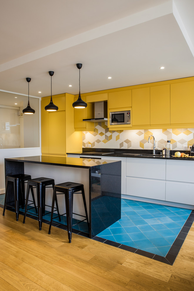 Medium sized scandinavian single-wall kitchen/diner in Paris with a double-bowl sink, yellow cabinets, yellow splashback, porcelain splashback, stainless steel appliances, ceramic flooring, an island, blue floors and black worktops.