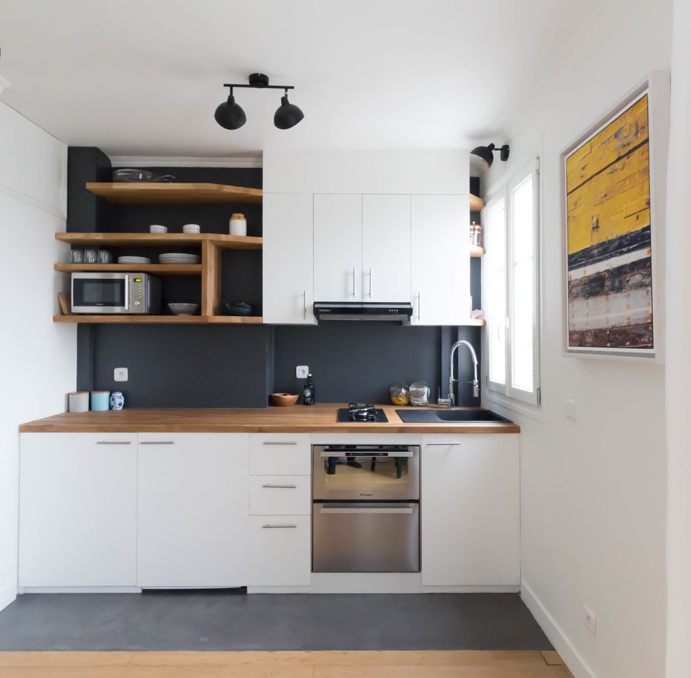 Exempel på ett litet modernt brun linjärt brunt kök och matrum, med en enkel diskho, vita skåp, träbänkskiva, svart stänkskydd, stänkskydd i skiffer, integrerade vitvaror, svart golv, släta luckor och betonggolv