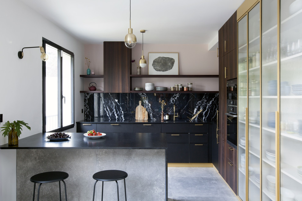 Moderne Küche mit flächenbündigen Schrankfronten, schwarzen Schränken, Küchenrückwand in Schwarz, Rückwand aus Stein, Halbinsel, grauem Boden und schwarzer Arbeitsplatte in Paris